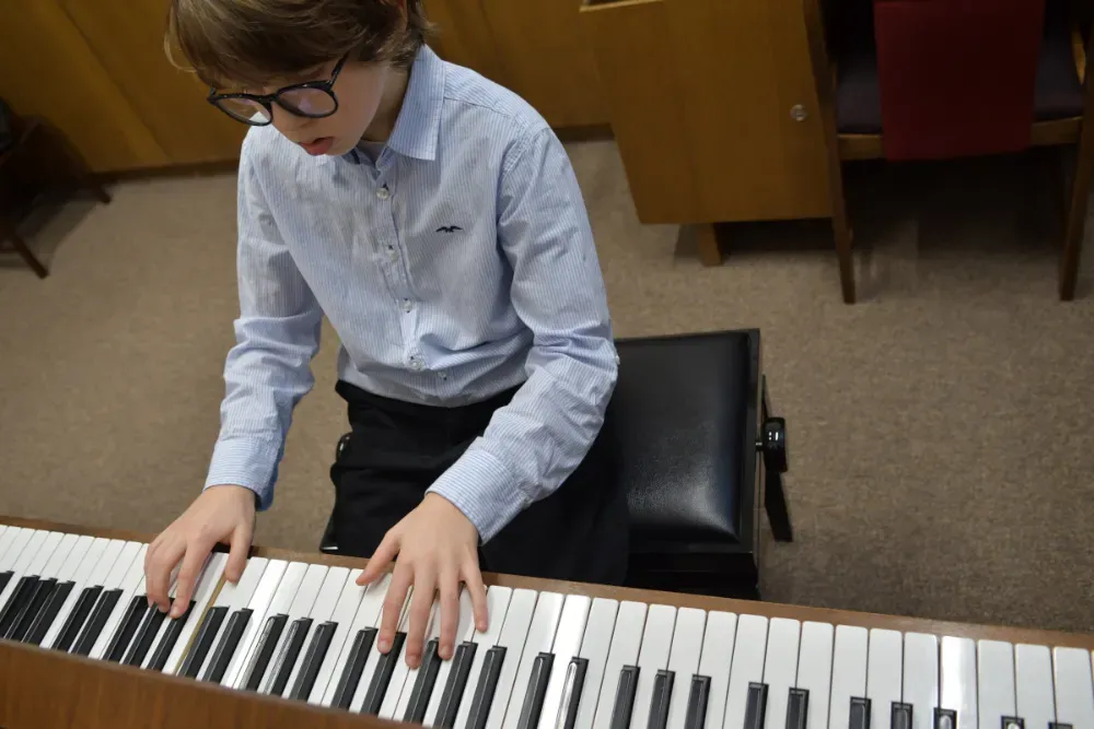 A student sitting at an upright piano during a lesson